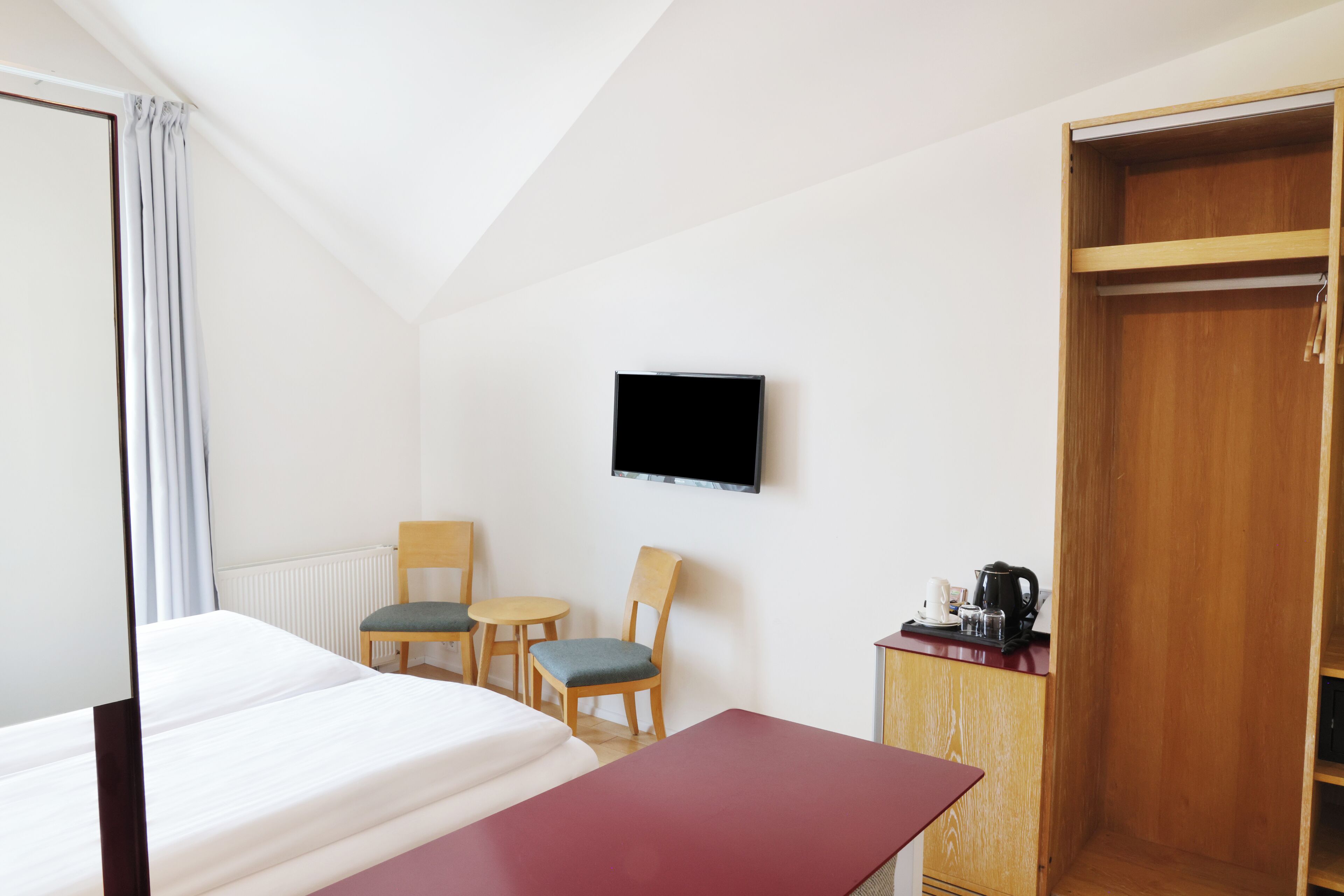 Una habitación de hotel con cama, escritorio, dos sillas, televisor, armario y cafetera.