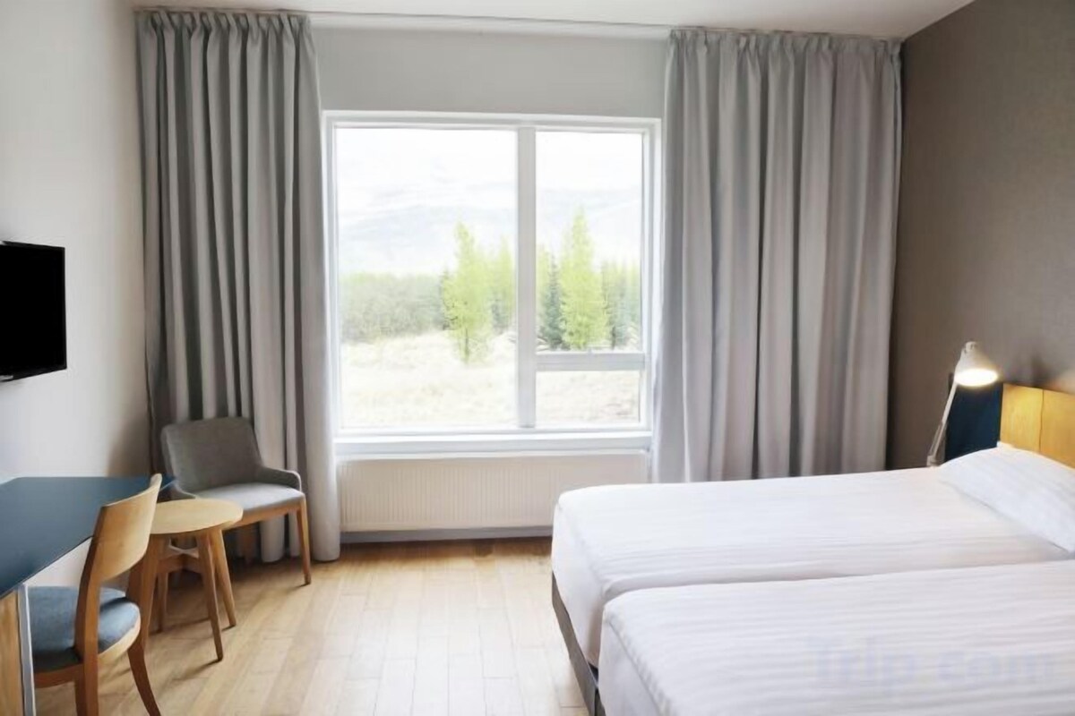 A hotel room with a bed, a desk, a chair, and a window with curtains.
