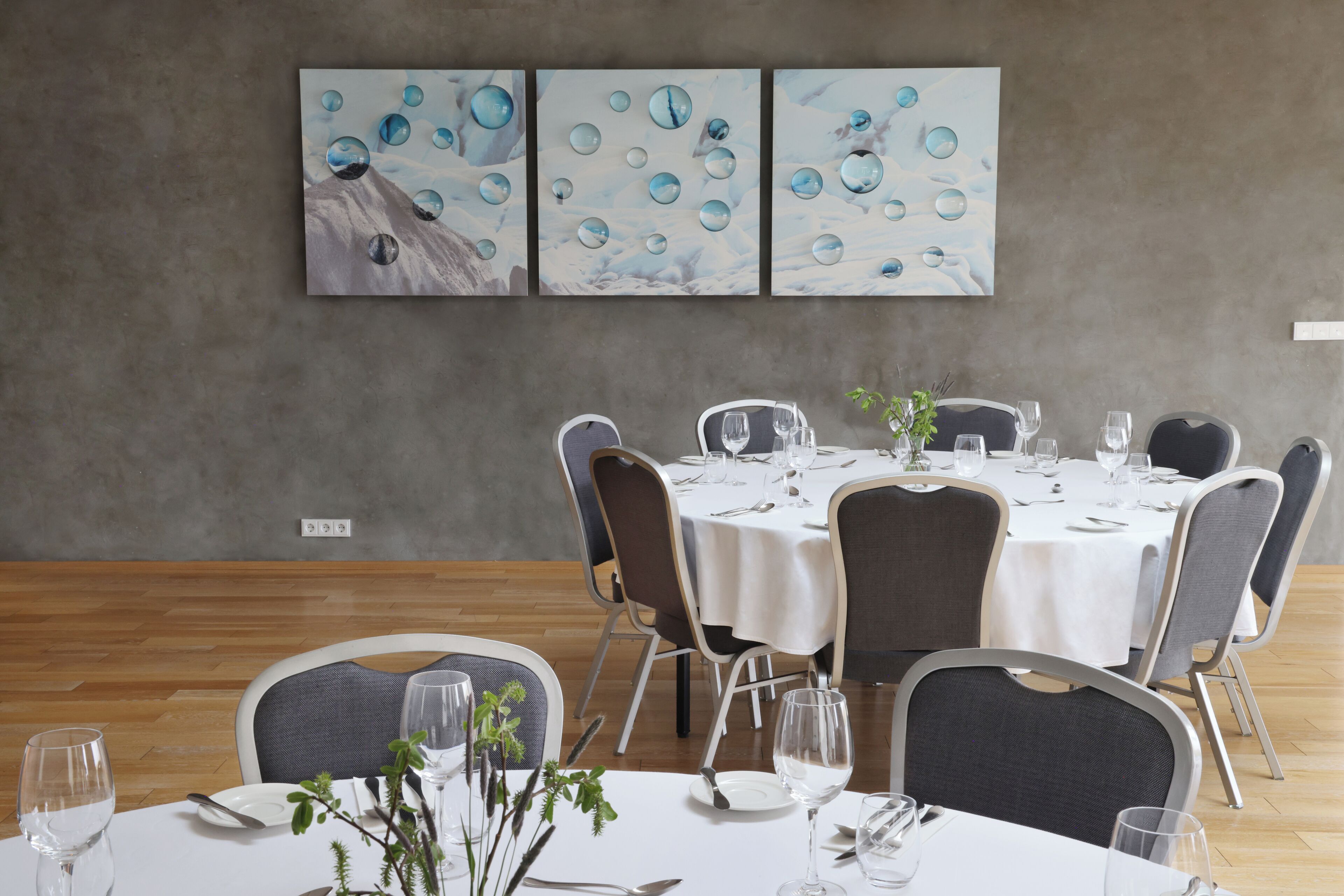 A dining area with round tables, chairs, and a wall-mounted painting.