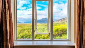Janela com vista para um campo verde e montanhas.