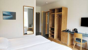 Habitación de hotel con una cama, un armario de madera, un escritorio con silla, un televisor y un cuadro en la pared.