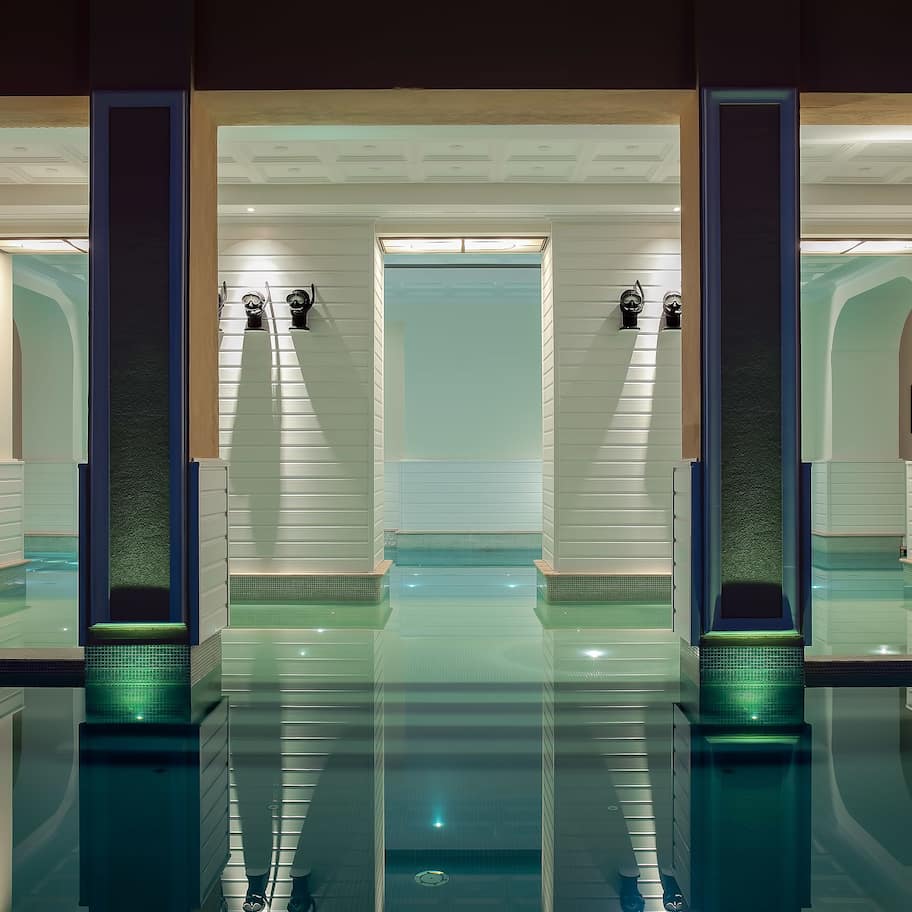 A modern hotel lobby with a central glass pool, mirrored walls, and framed artwork on the walls.
