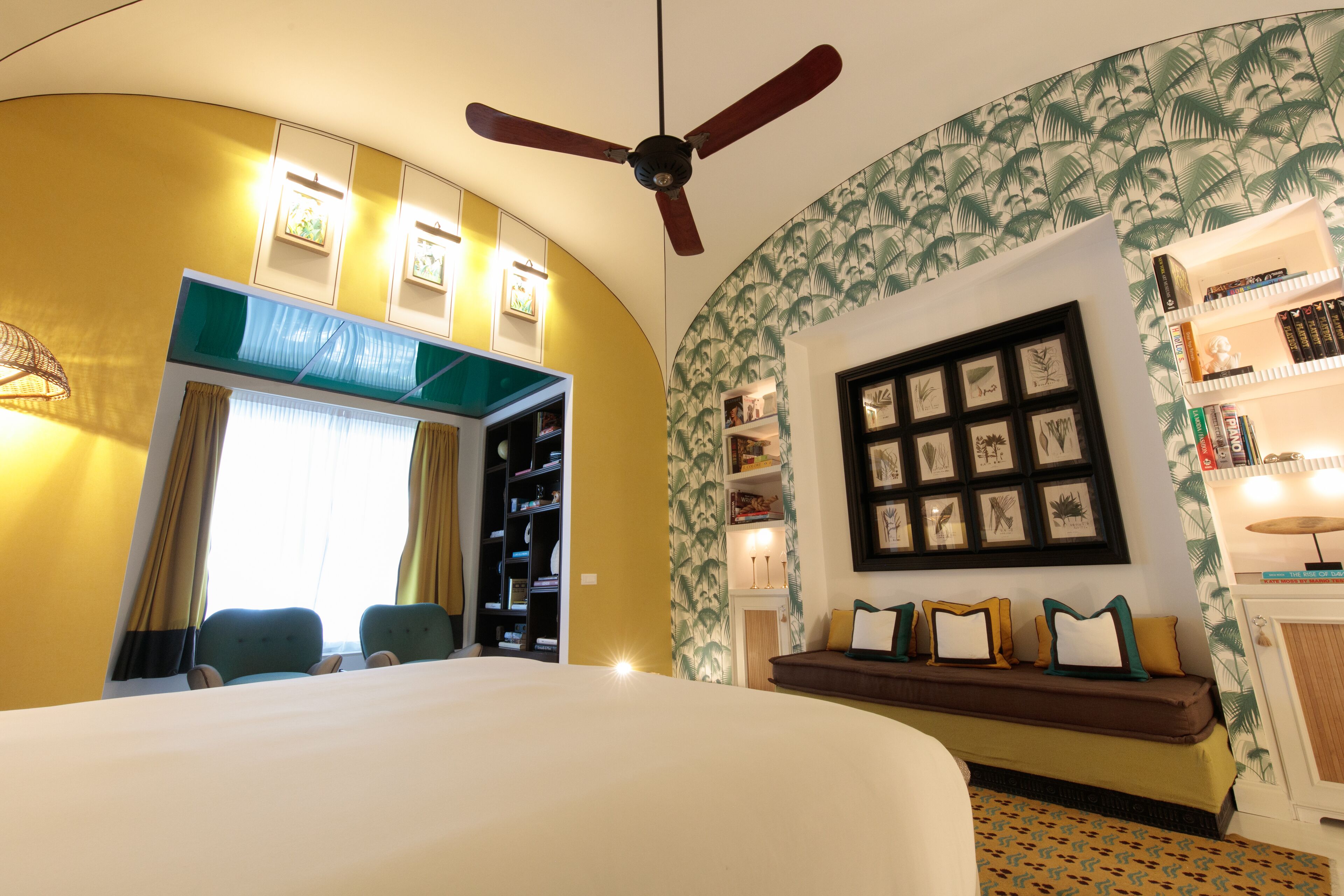 Una habitación de hotel con techo curvo, una cama, zona de estar con un banco, ventilador de techo y estantería.