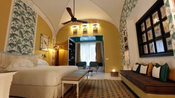Una habitación de hotel con cama, sofá, ventilador de techo y alfombra estampada.