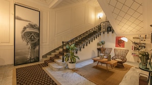 Un hall d’entrée spacieux doté d’un sol en marbre, d’un grand tableau abstrait, d’un escalier avec des rampes décoratives et d’un coin salon avec une table et des chaises.