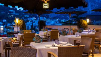 Enjoy al fresco dining with a city view, surrounded by elegant table settings and comfortable wicker chairs.