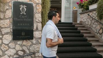 Un homme se tient à l’entrée du Capri Tiberio Palace, à côté d’un panneau indiquant le nom de l’établissement et sa note de 5 étoiles.