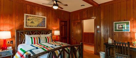 A wooden-paneled room with a bed, a desk, and a chair.