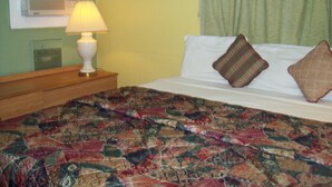 A bed with a patterned bedspread, a bedside lamp, and two pillows. - Budget Inn Sanderson (Sanderson)
