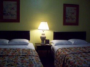 A hotel room with two beds, each with floral bedding, a nightstand with a lamp, and framed artwork on the walls.