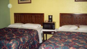 A hotel room with two beds, a wooden headboard, a small table with a microwave, and a painting on the wall.
