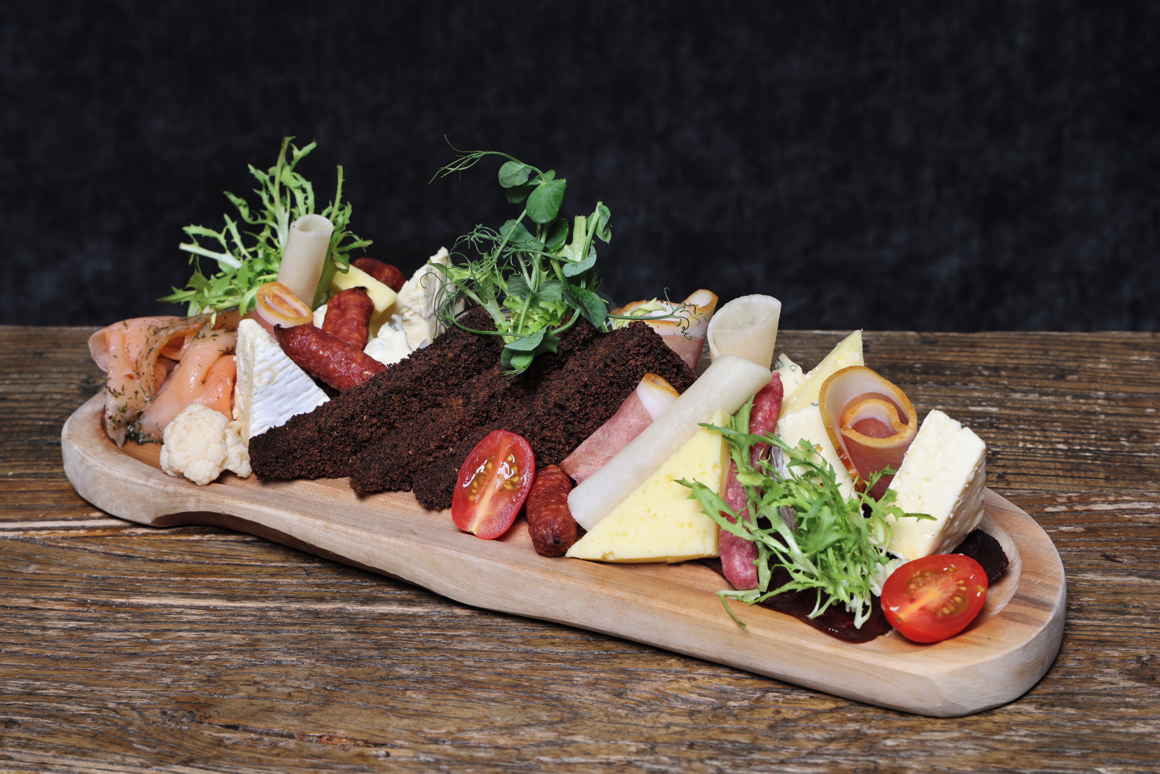 A wooden board with various cheeses, meats, and vegetables.