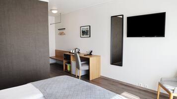 Quarto de hotel moderno com cama, escrivaninha, cadeira, televisão e um quadro na parede.