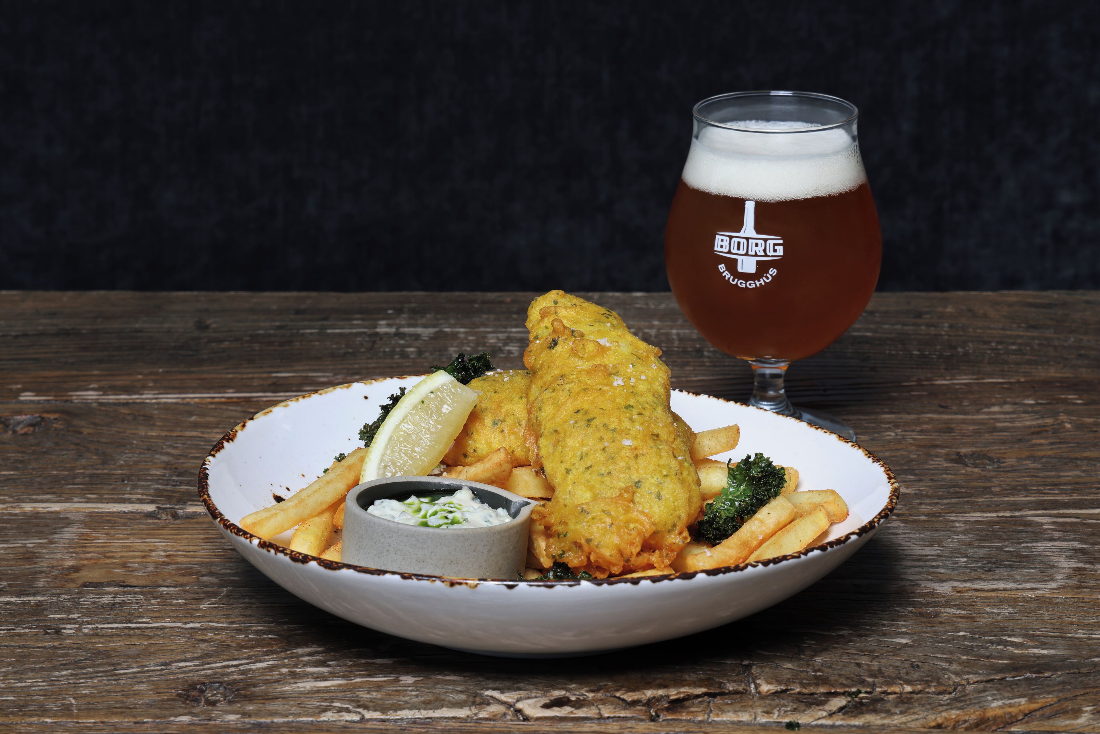 Un plato de pescado con patatas fritas y una cerveza sobre una mesa de madera.