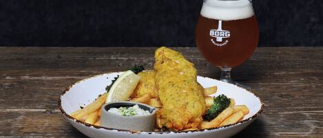 Un plato de pescado con patatas fritas y una cerveza sobre una mesa de madera.