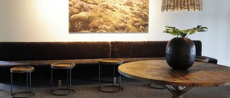 En mysig sittgrupp med ett runt träbord, tre pallar, en stor vas med en växt och en hängande lampa av rotting.