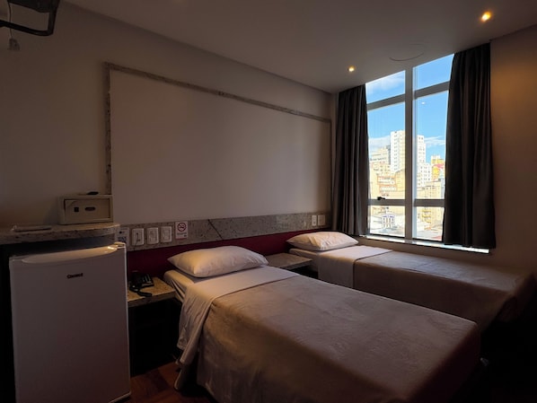 Habitación de hotel con dos camas, refrigerador, microondas, teléfono y ventana con vista a la ciudad.
