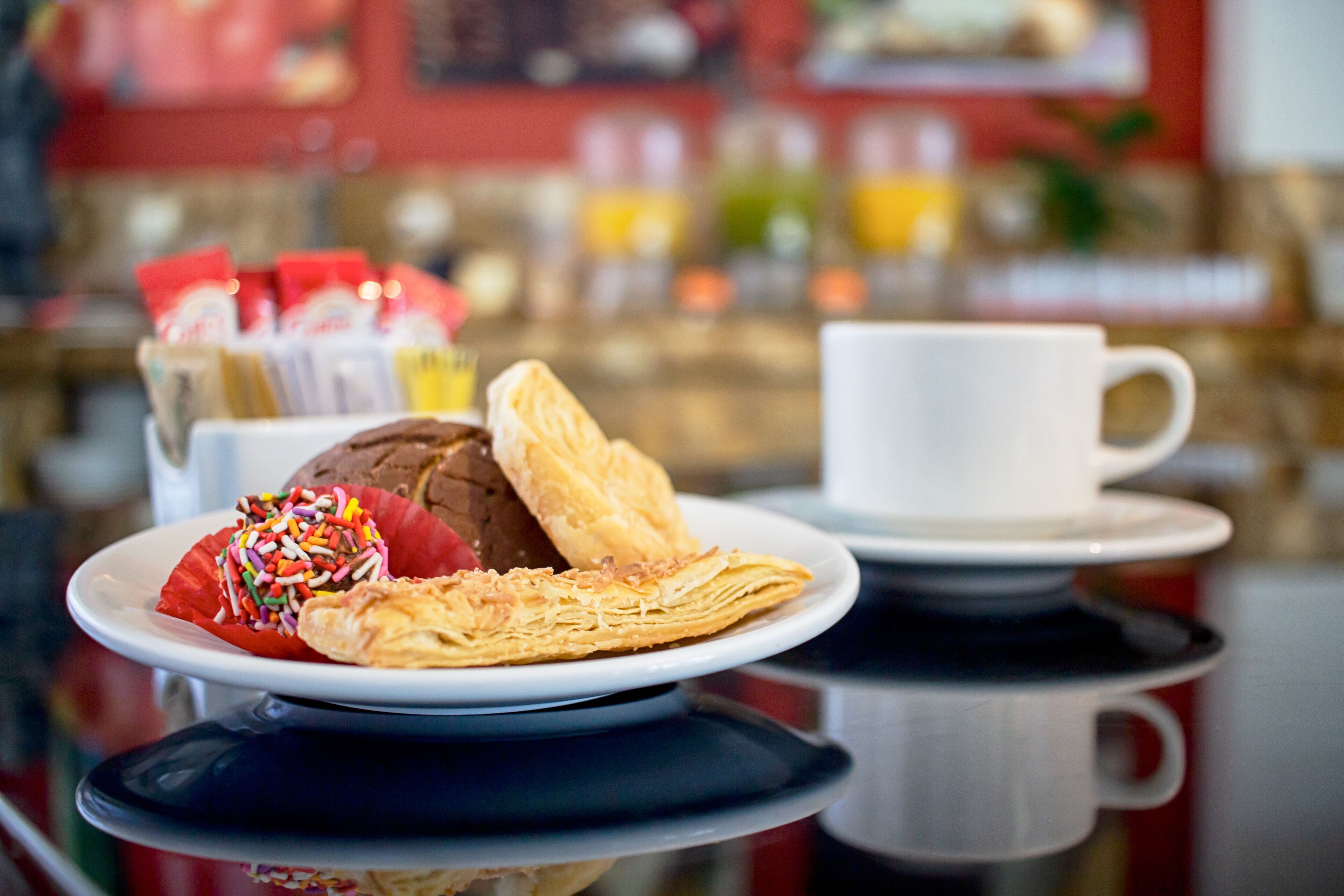 A breakfast setting with a plate of pastries, a cup, and a glass of orange juice on a reflective surface.