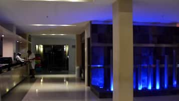 Un vestíbulo de hotel con mostrador de recepción, un pilar grande y una fuente iluminada en azul.