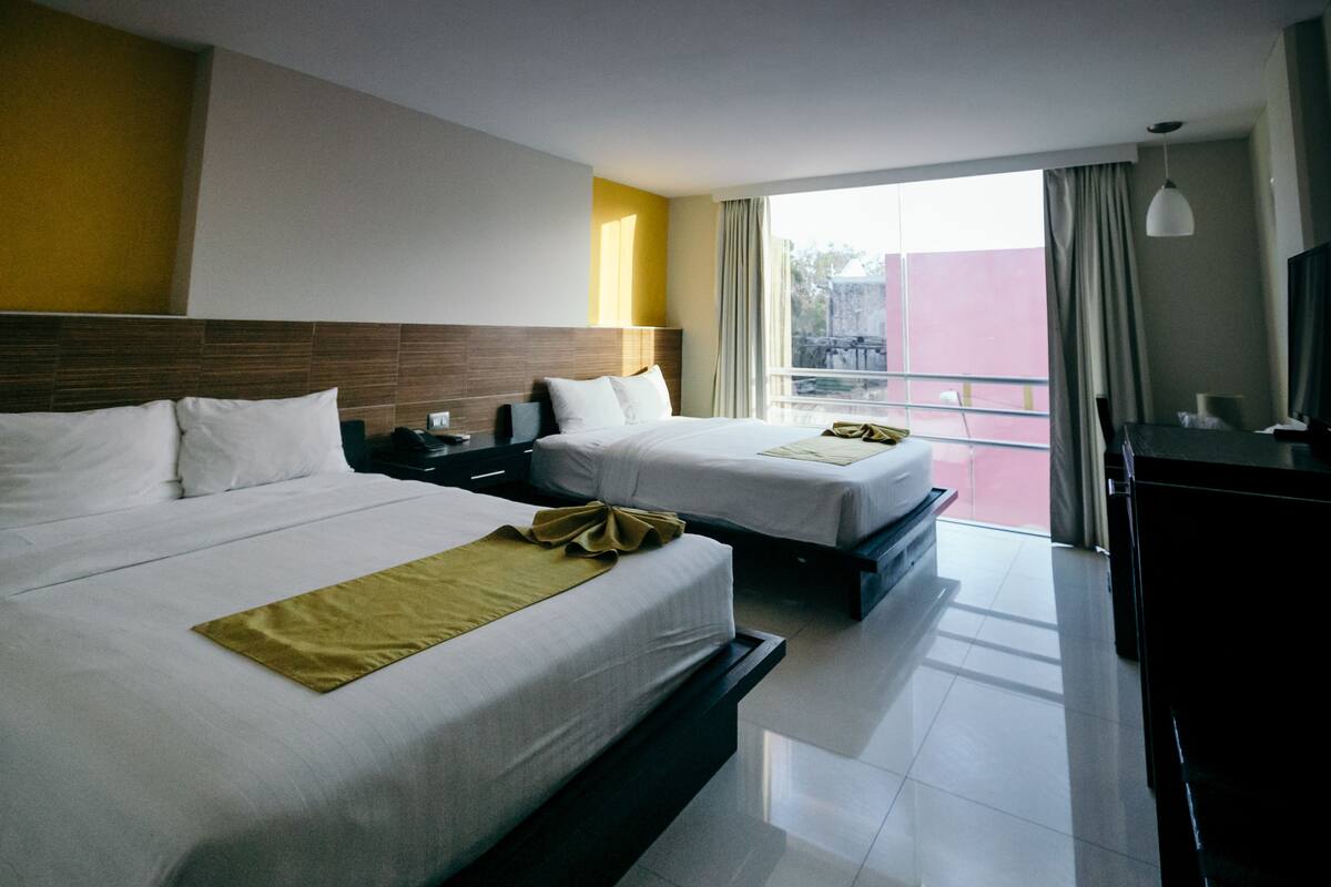 A hotel room with two beds, a desk, and a large window.