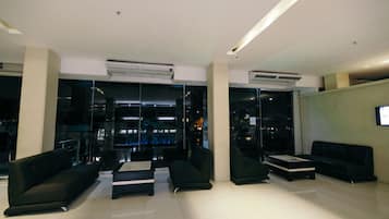 Un vestíbulo moderno con sofás negros, una mesa de centro y paredes de vidrio que ofrecen vistas de la ciudad de noche.