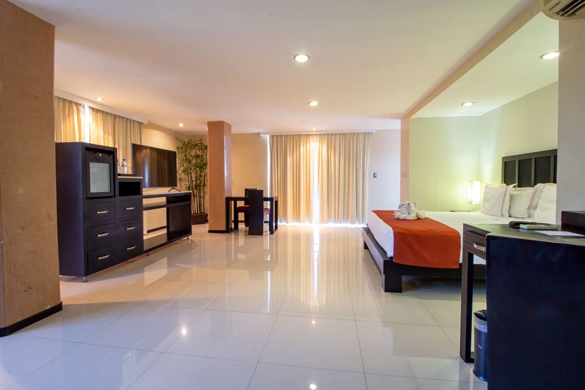A hotel room with a bed, desk, chair, and a TV on a cabinet.
