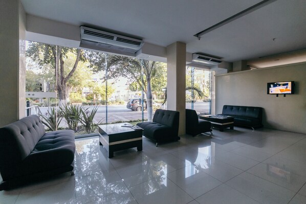 Un vestíbulo moderno con pared de vidrio, televisor de pantalla plana y arreglos de asientos.
