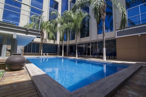 Piscina interior moderna con agua azul cristalina, rodeada de palmeras y una terraza de madera.