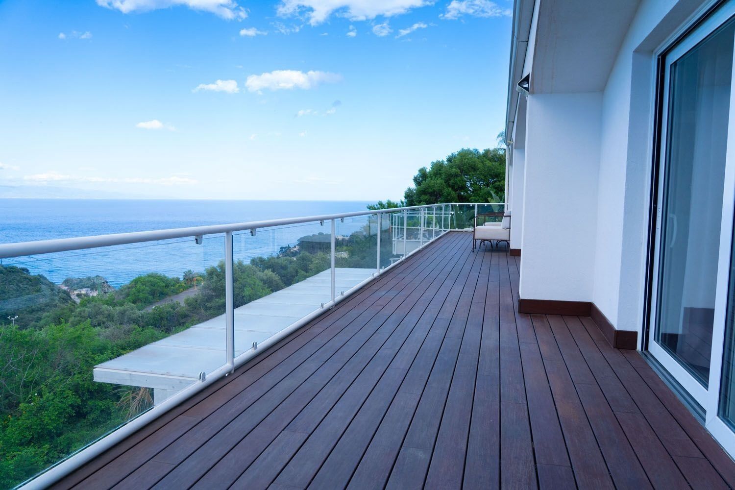 A wooden deck with a glass balustrade overlooking a coastal view.