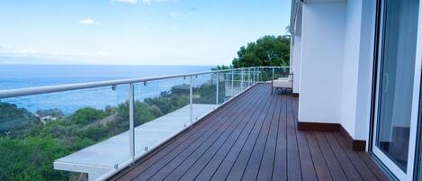 A wooden deck with a glass balustrade overlooking a coastal view.