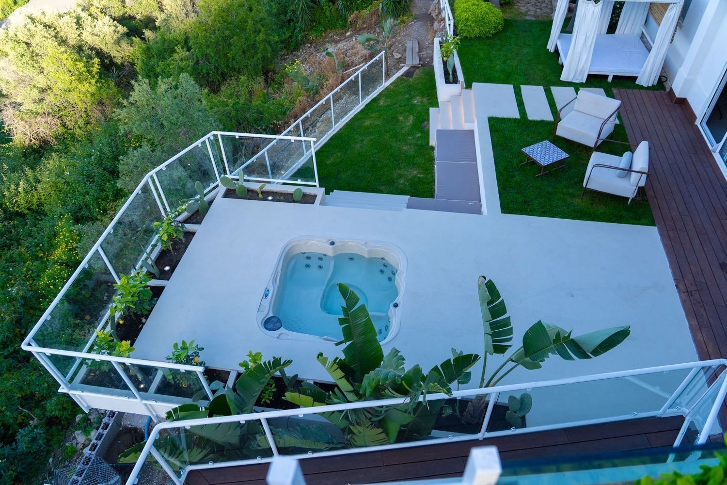 Luchtbeeld van een terras op het dak met een jacuzzi, omgeven door een glazen balustrade, grenzend aan een gazon met buitenmeubilair.