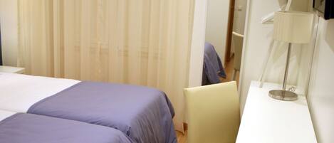 A hotel room with two beds, a desk, a chair, a lamp, and a mirror.