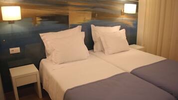Cama doble con ropa blanca y dos almohadas, una mesita de noche y una lámpara de pared.