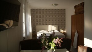 Ein Schlafzimmer mit strukturiertem Wandpapier, einem Bett mit weißer Bettwäsche, einem Nachttisch mit Lampe und einer Vase mit Blumen.
