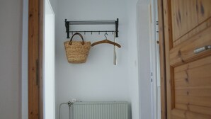Ein schmaler Flur mit Heizkörper, Holzrahmen einer Tür und einer Kleiderstange mit Korb und Kleiderbügel.