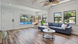 Un salon spacieux doté d’un plancher en bois franc, d’un canapé gris, d’une table basse ronde et d’un ventilateur de plafond.