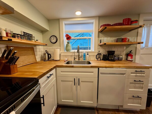 A kitchen with white cabinets, a stainless steel sink, wooden countertops, and a window with a view.