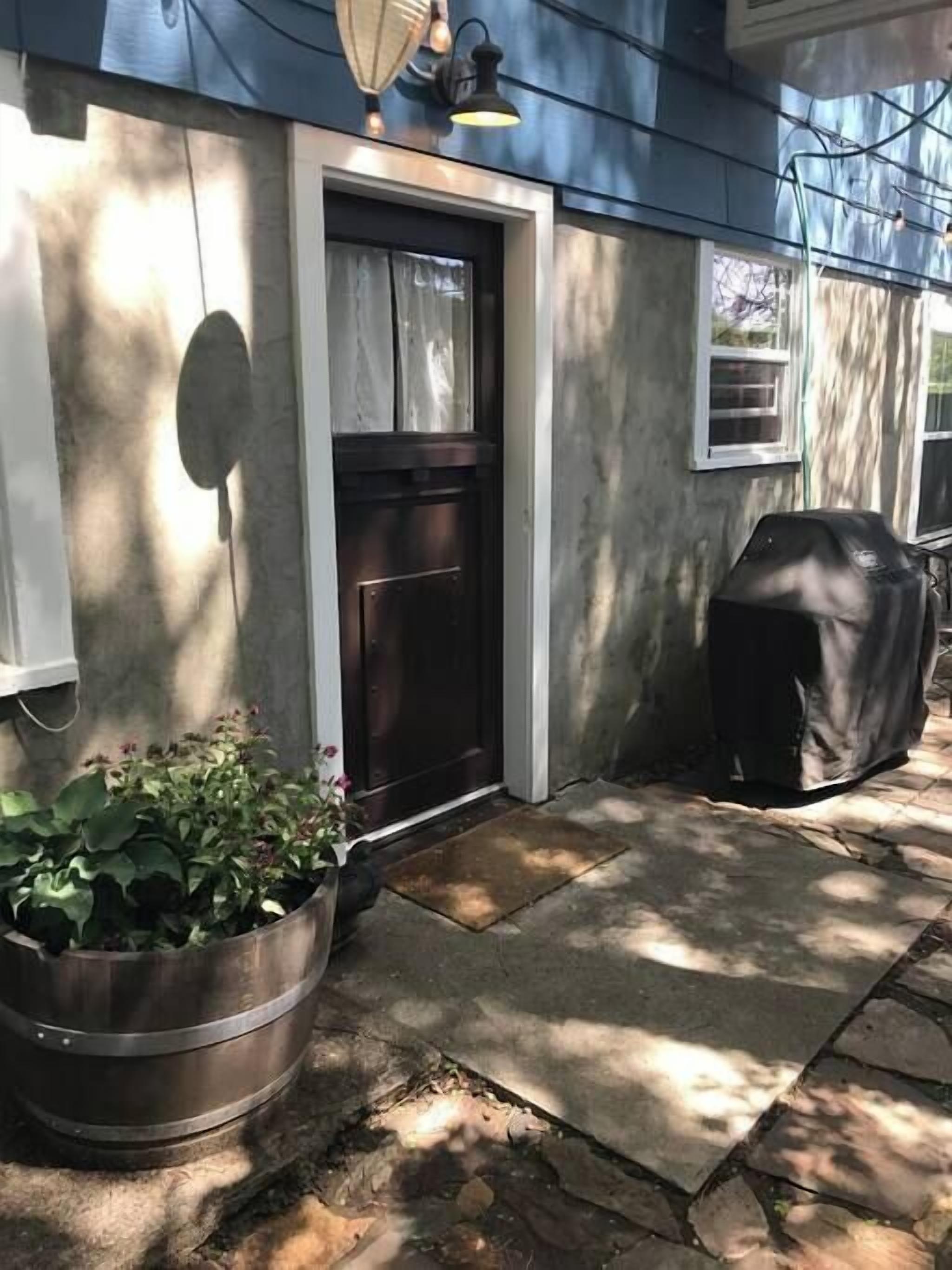 Une maison avec une porte d’entrée sombre, un pot de fleurs et un espace barbecue abrité.