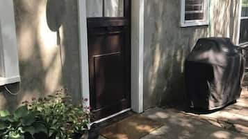 Une maison avec une porte d’entrée sombre, un pot de fleurs et un espace barbecue abrité.