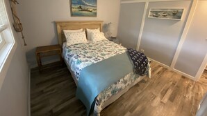 Une chambre avec un lit en bois, une table de chevet, un banc, un mur décoré d’œuvres d’art sur le thème de la marine, et un plancher en bois.