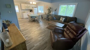 Un salon spacieux avec un canapé en cuir marron, une table basse en bois et un coin repas avec une nappe bleue.