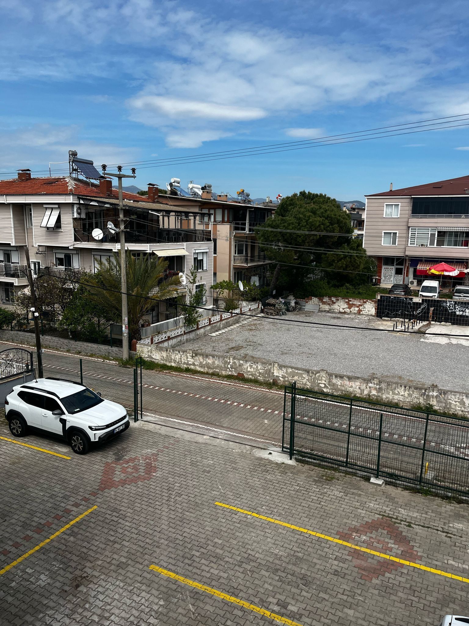 Un área de estacionamiento con un coche blanco, edificios con balcones y un cielo despejado.