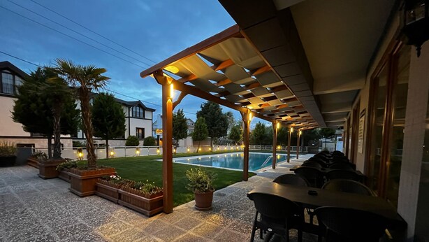 An outdoor patio area with a pool, seating, and a pergola with lights. - Akcay Zeytin Otel (Edremit)