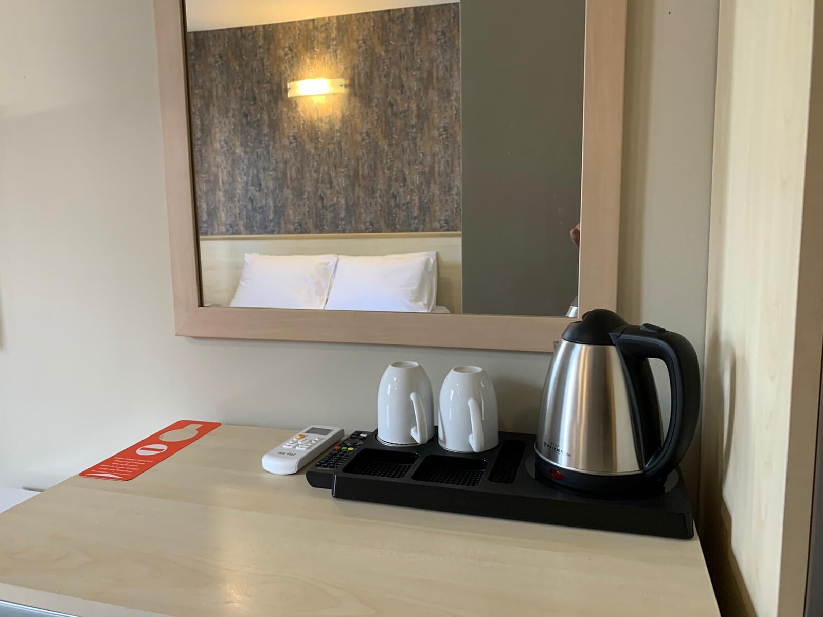 Une chambre d’hôtel avec un lit, une table de chevet avec une bouilloire, deux tasses et une télécommande.