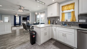 A modern kitchen with white cabinets, a granite countertop, and a built-in oven. There is a dining area with a table and chairs, and a ceiling fan. - Parrot Bay 2 bedroom Condo in Downtown OC with pool near the beach (Ocean City)