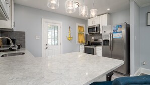 A modern kitchen with a marble countertop, stainless steel appliances, pendant lights, and a yellow curtain. - Parrot Bay 2 bedroom Condo in Downtown OC with pool near the beach (Ocean City)