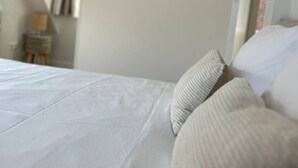 A neatly made bed with white linens and striped pillows in a room with a white door and a wall-mounted fruit decoration.