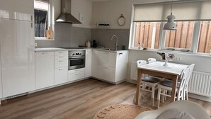 A modern kitchen with white cabinets, a built-in oven, and a dining area with a table and chairs.
