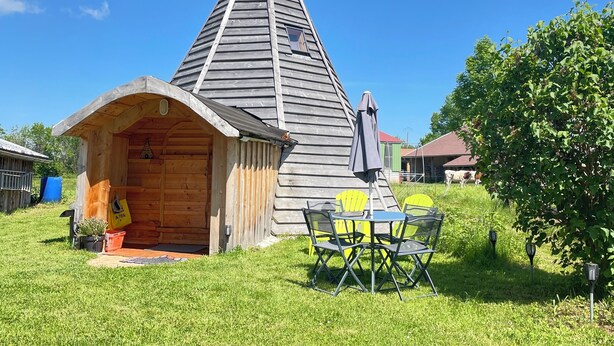 Een houten blokhut met een puntdak, een klein terras en een tafel met stoelen.