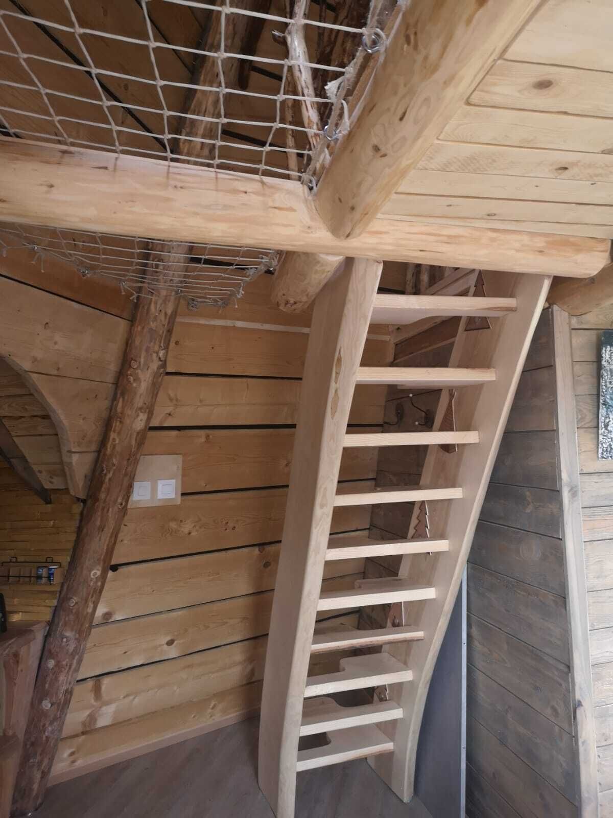 Interior de madera con una escalera de madera y un techo con vigas a la vista.